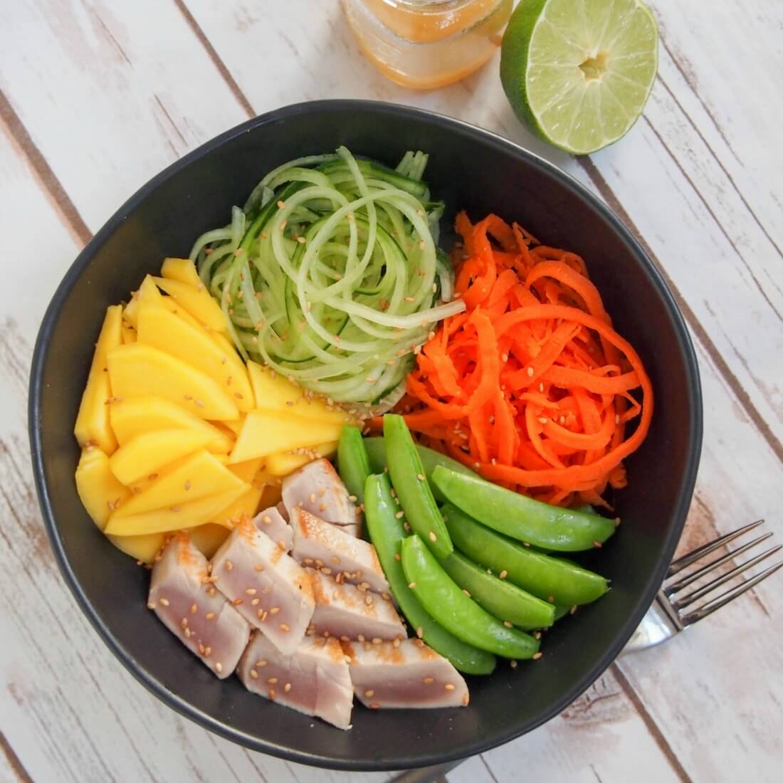 Seared tuna and veggie bowl with half lime and additional dressing to top of bowl viewed from above
