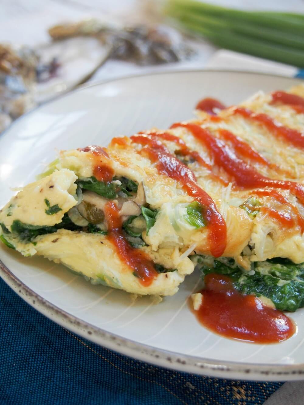 Taiwanese oyster omelette is a classic street food, but it also makes a delicious brunch/lunch - easy to make and with lots of great flavor, with oysters, greens and a flavorful sauce. close up view of omelette showing filling with sauce dripping over top