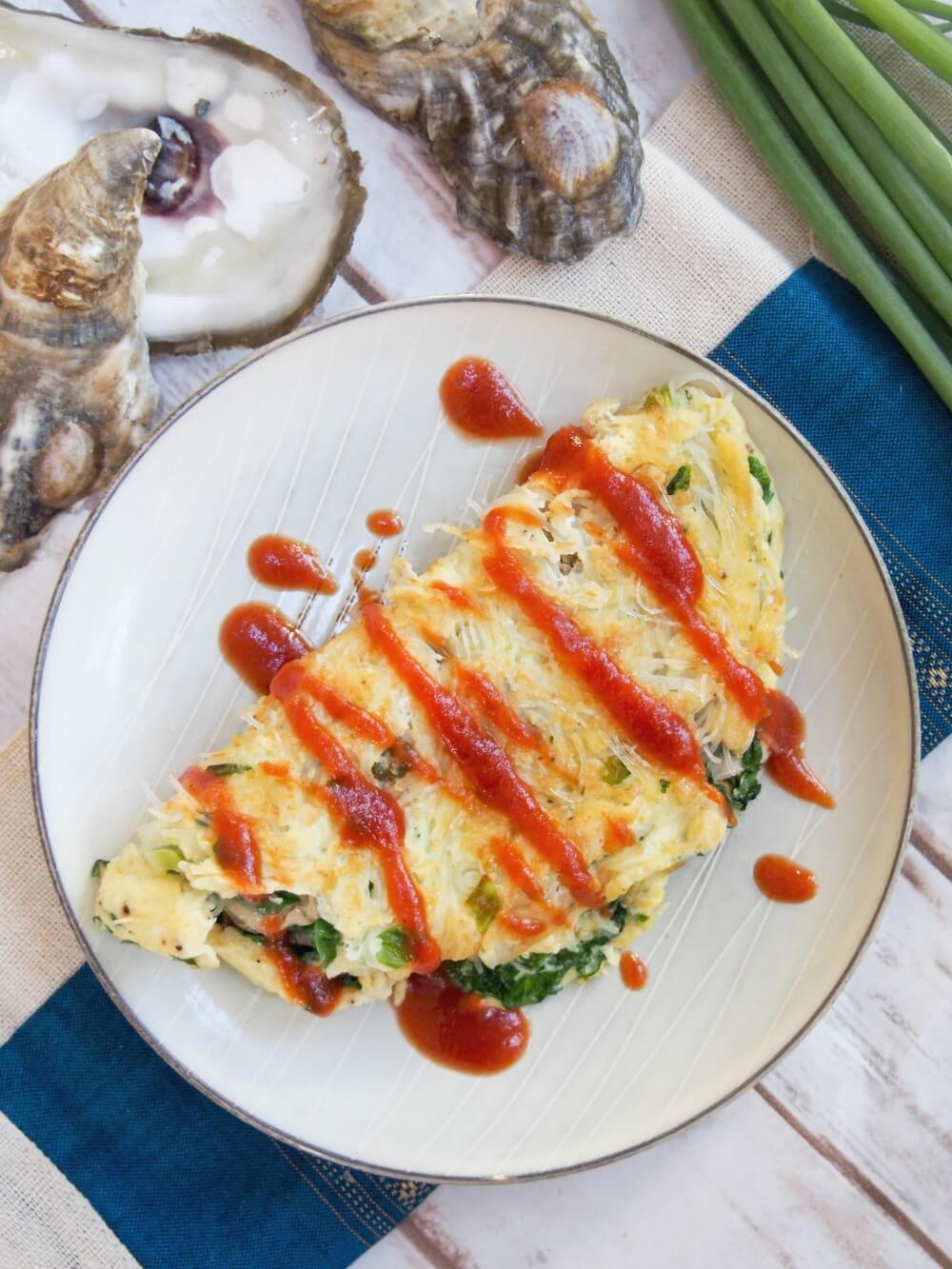 Taiwanese oyster omelette is a classic street food, but it also makes a delicious brunch/lunch - easy to make and with lots of great flavor, with oysters, greens and a flavorful sauce. Taiwanese oyster omelette viewed from overhead with oyster shells above plate