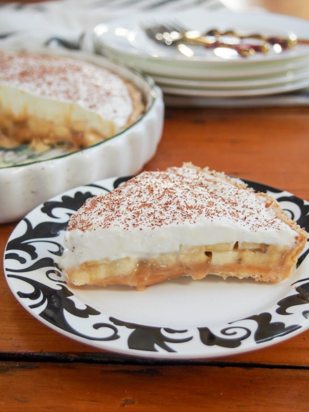 slice of banoffee pie in front of rest of pie and serving plates in background