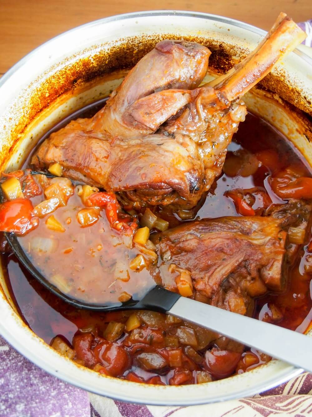 braised lamb shanks in pot just out oven with spoon in pot scooping some sauce