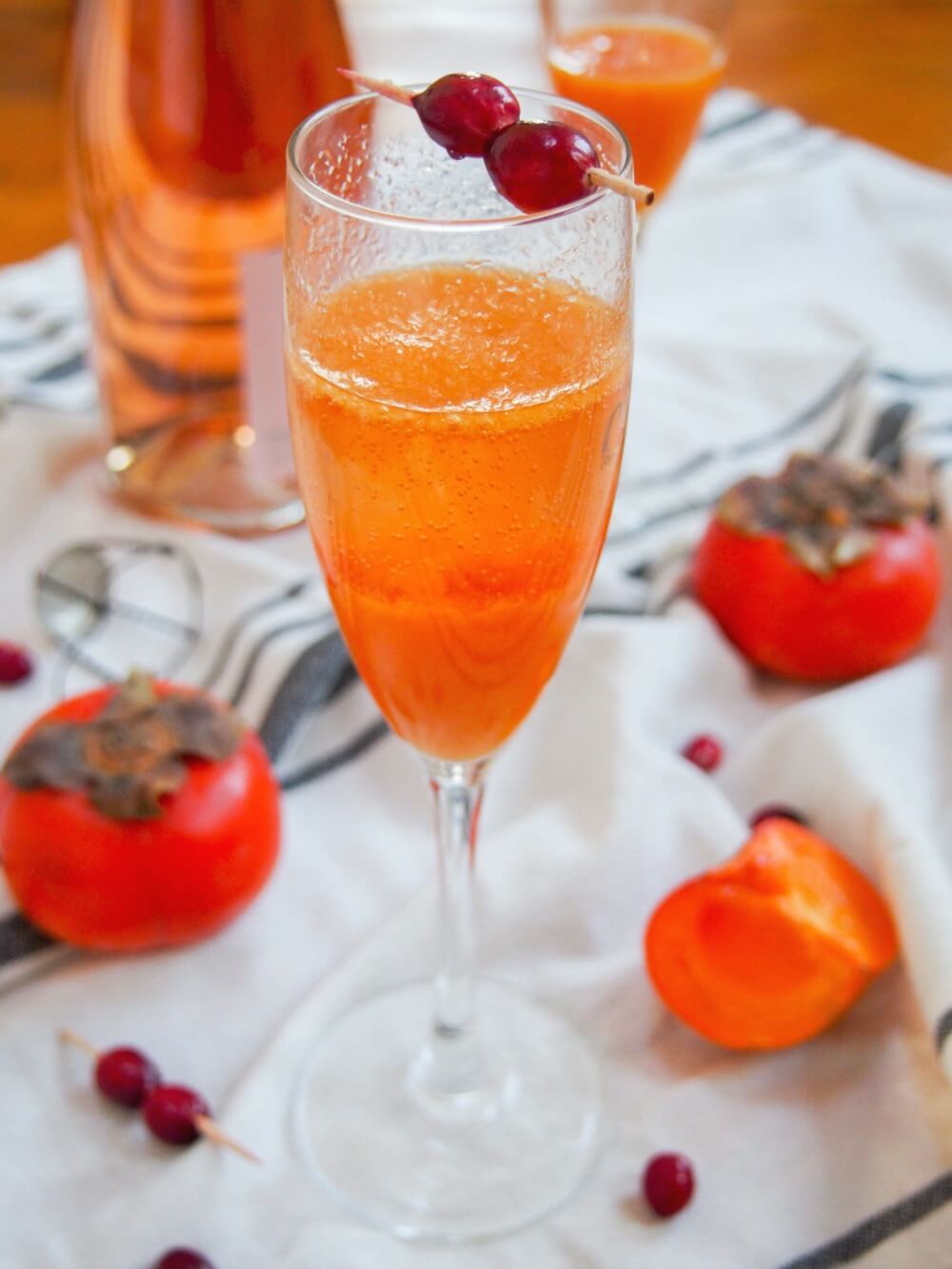 glass of persimmon apple cider mimosa with bubbles settled and cranberry garnish