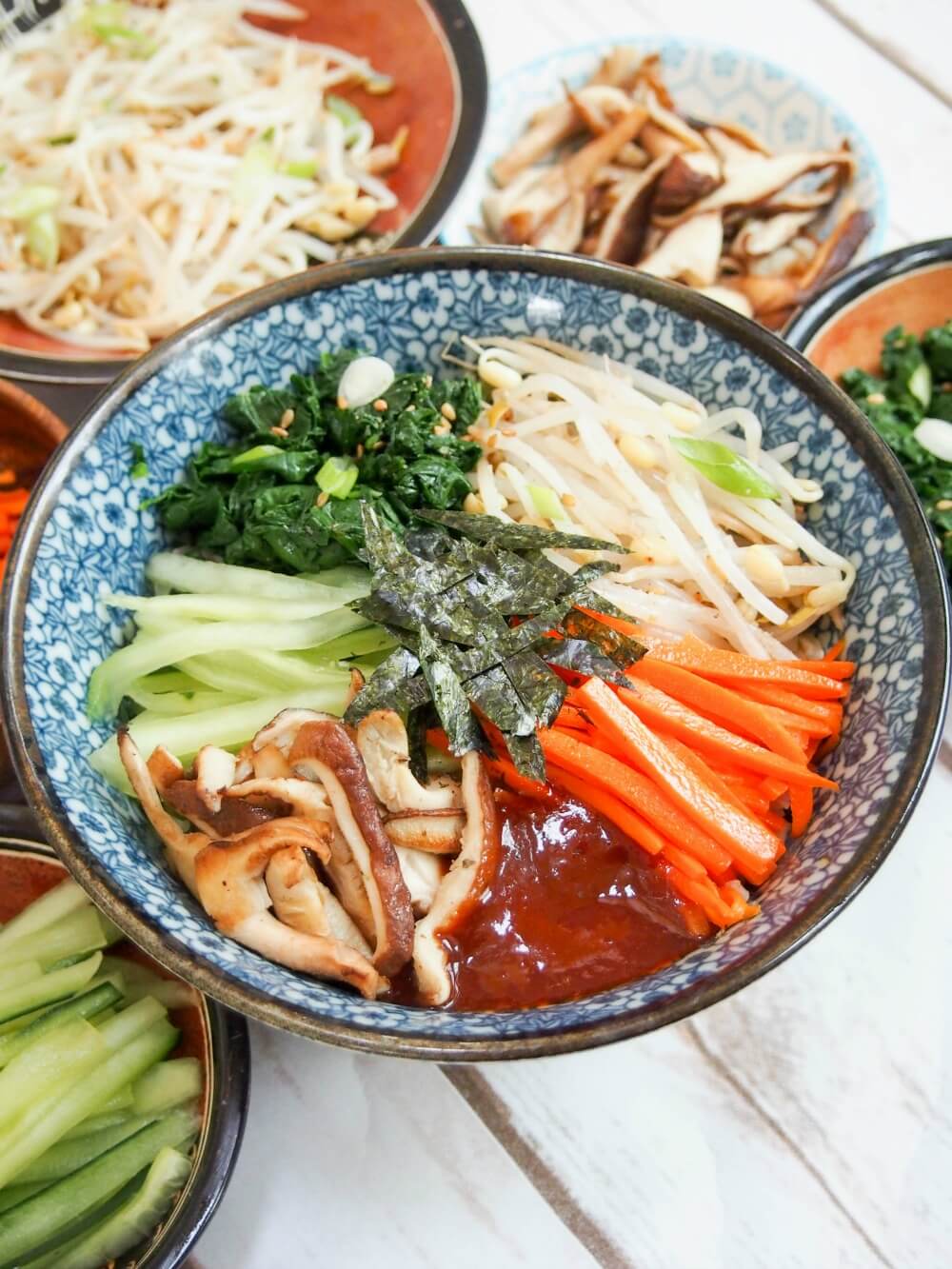 bowl of vegetarian bibimbap with some of vegetables in small bowls around main bowl