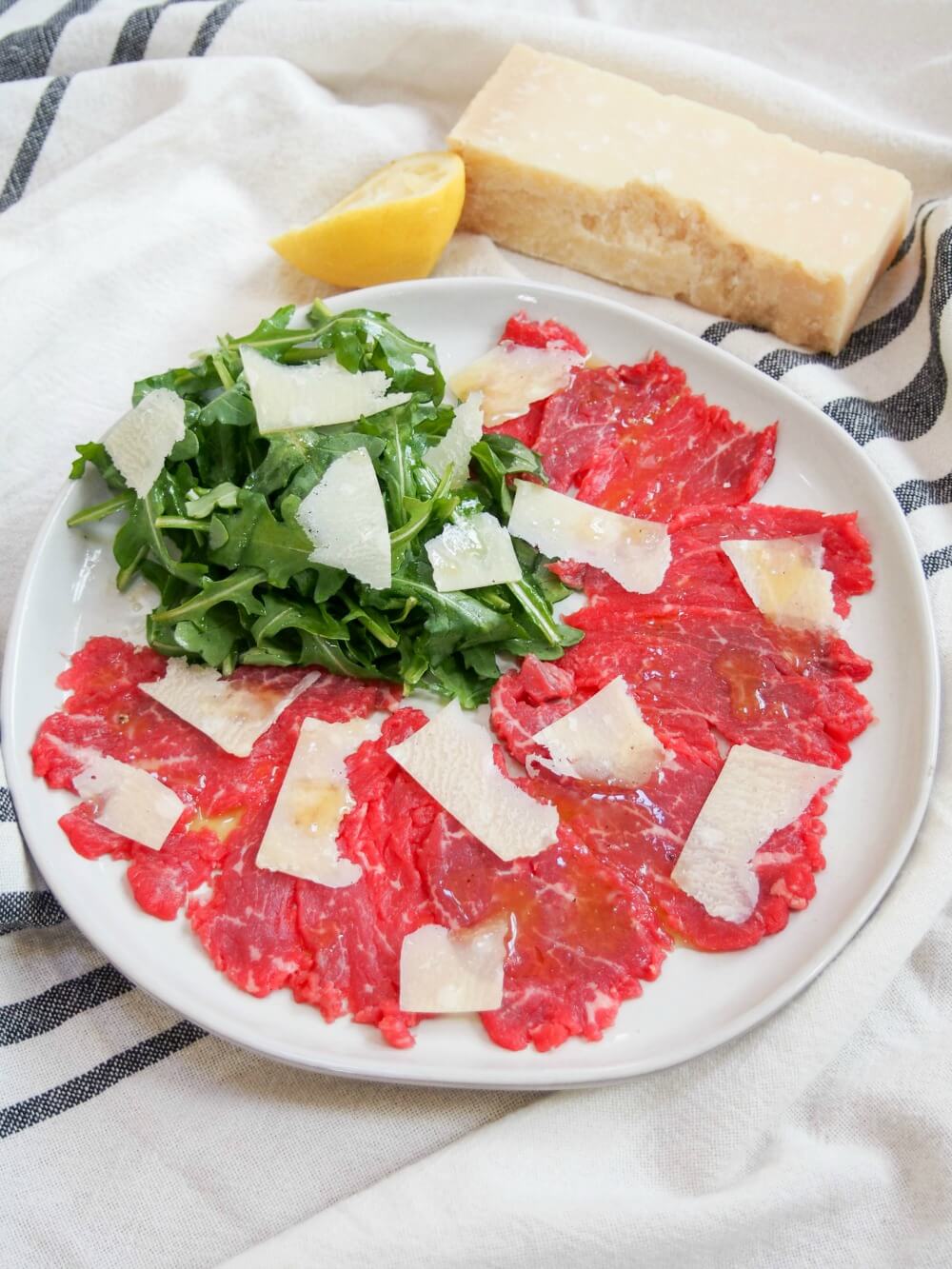 slices of beef carpaccio topped with shaved parmesan and arugula salad to side