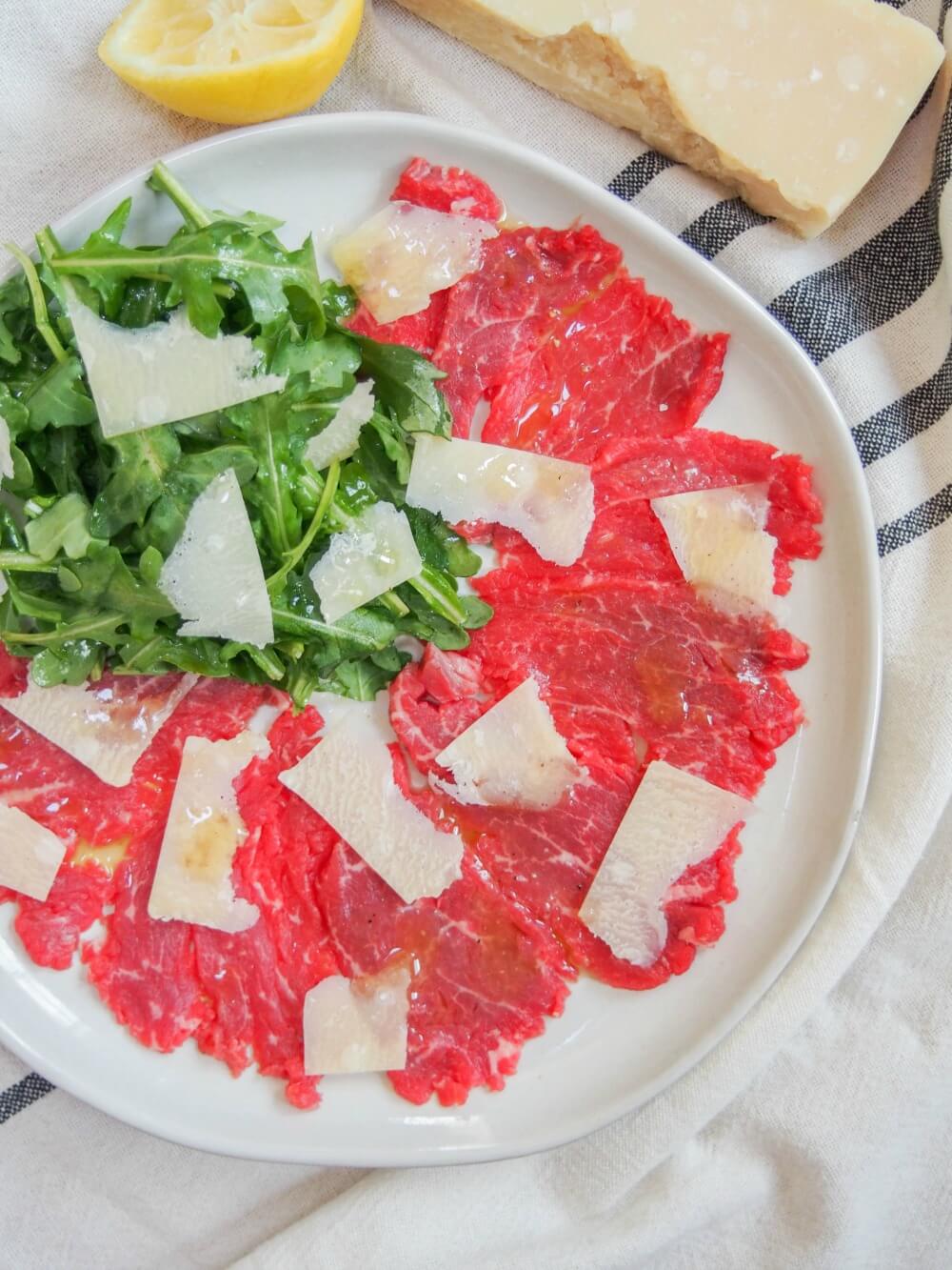Beef carpaccio with truffle vinaigrette and parmesan slices on top viewed from overhead