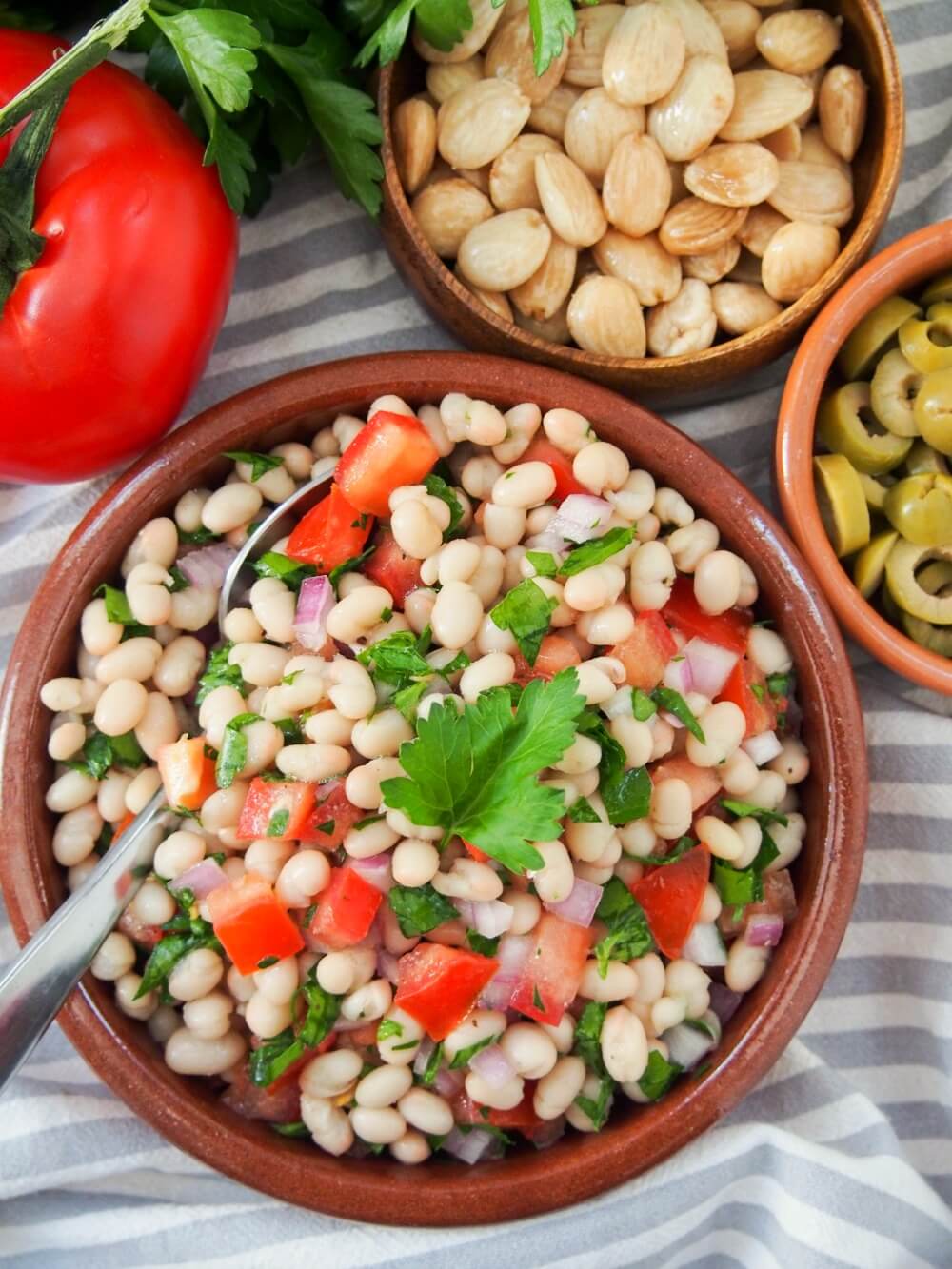 Easy white bean salad from overhead with almonds, olives and tomato on side