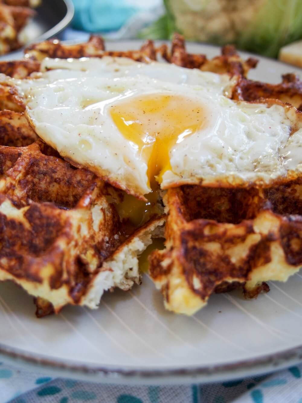 These cauliflower waffles need only 5 ingredients and are quick to make. They make a tasty, low carb and gluten free any-time snack/ light meal. Cauliflower waffles with cut egg on top and yolk oozing into waffle
