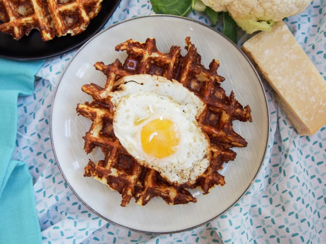 Cauliflower waffles are cheesy and tasty! Cauliflower waffle on plate with egg on top and cheese block to side