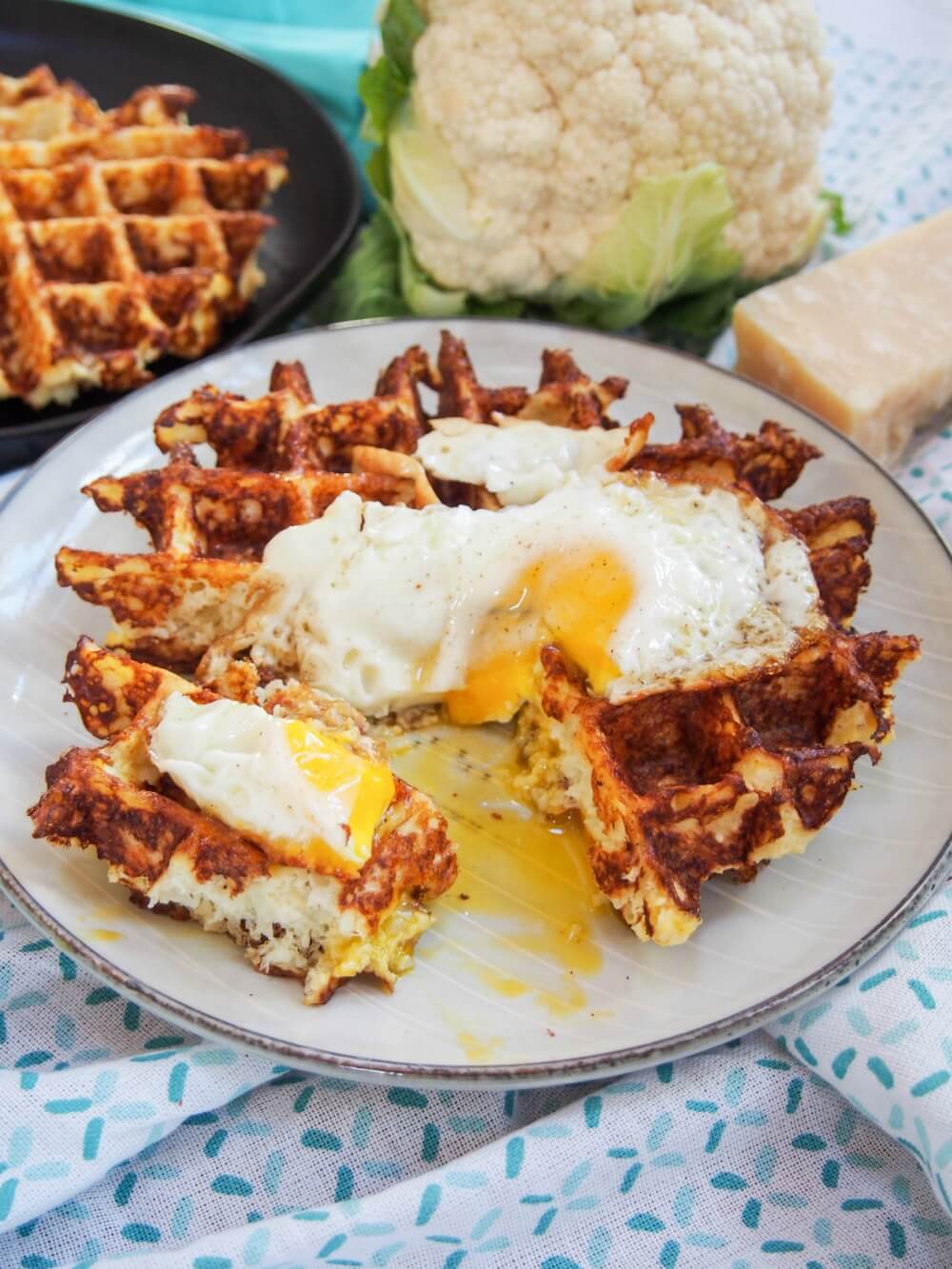 These cauliflower waffles need only 5 ingredients and are quick to make. They make a tasty, low carb and gluten free any-time snack/ light meal. Cauliflower waffle with egg on top and quarter cut out from it