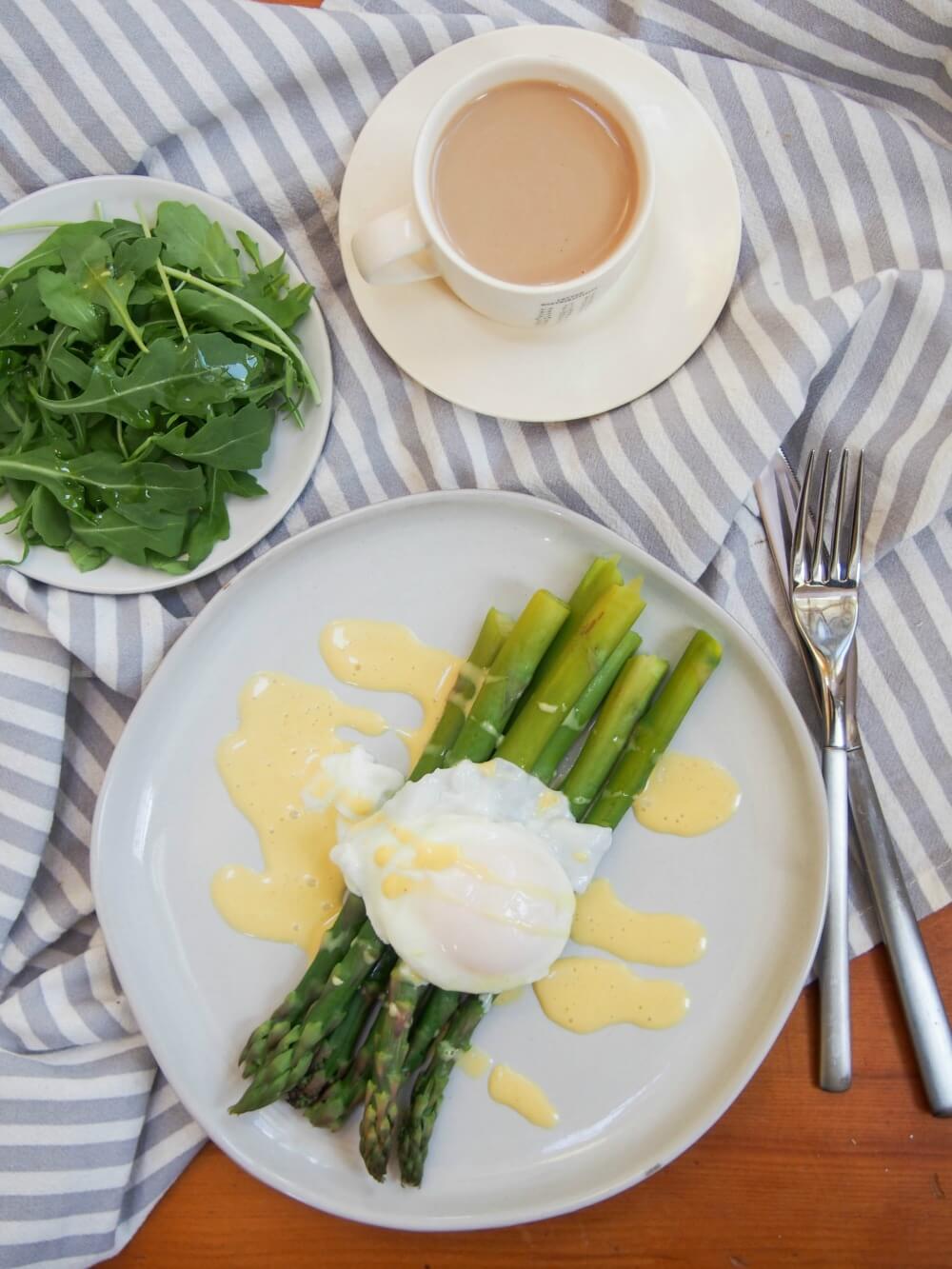 Asparagus with hollandaise sauce and poached egg with plate of side salad and cup of coffee above overhead view