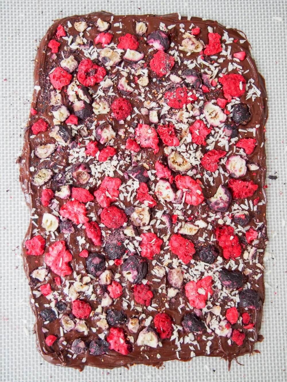 adding toppings to melted chocolate for blueberry raspberry chocolate bark