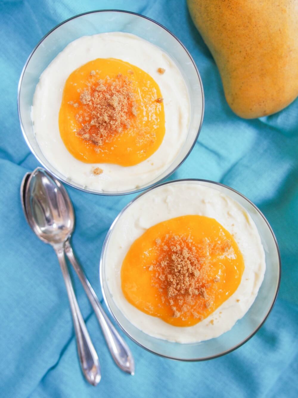 two glasses of mango cheesecake parfait from overhead with spoons to side