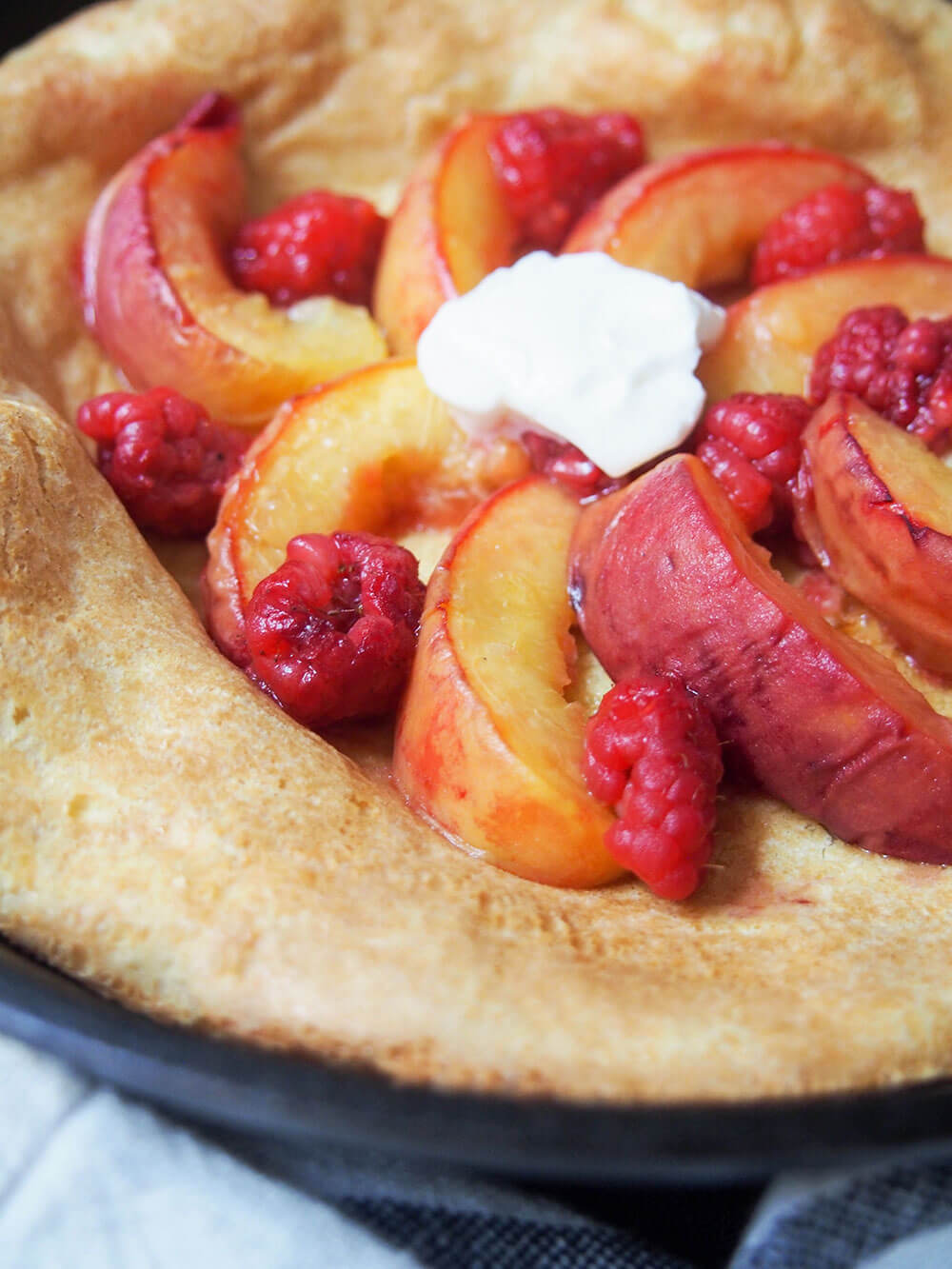 If you're looking for an easy breakfast/brunch that's packed with flavor, this peach Dutch baby pancake has to be high up the list. The roast peaches take this simple baked pancake from good to amazingly delicious! peach Dutch baby pancake side view with fruit on top of pancake