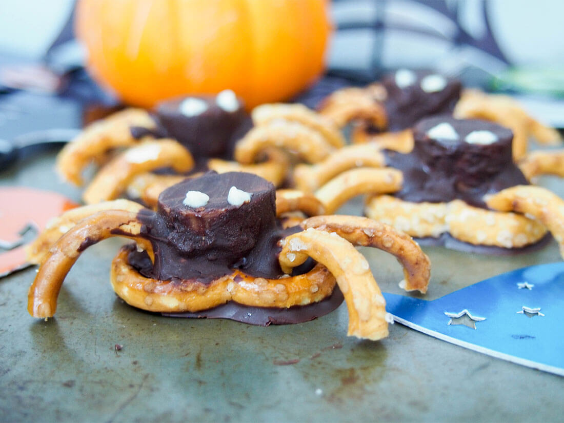 chocolate pretzel spiders with pumpkin behind