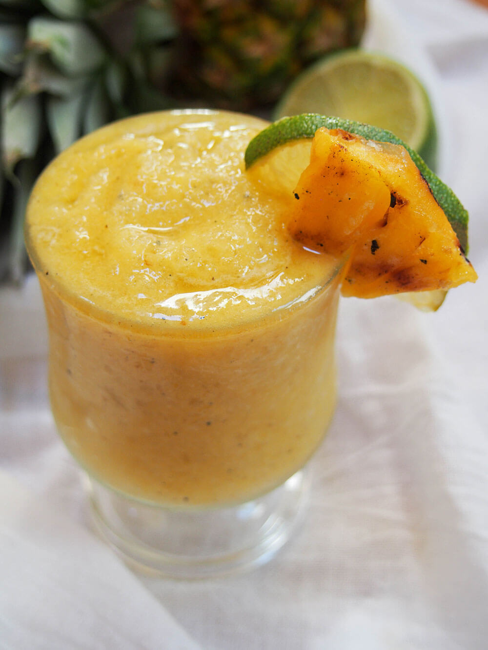 glass of frozen pineapple daiquiri with grilled pineapple and lime garnish