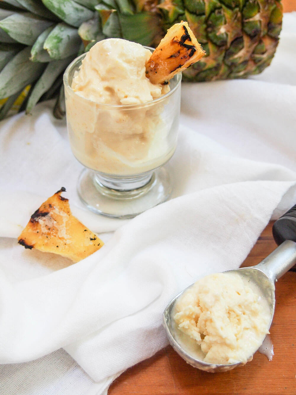 grilled pineapple ice cream in glass with piece of grilled pineapple to side and scoop in front