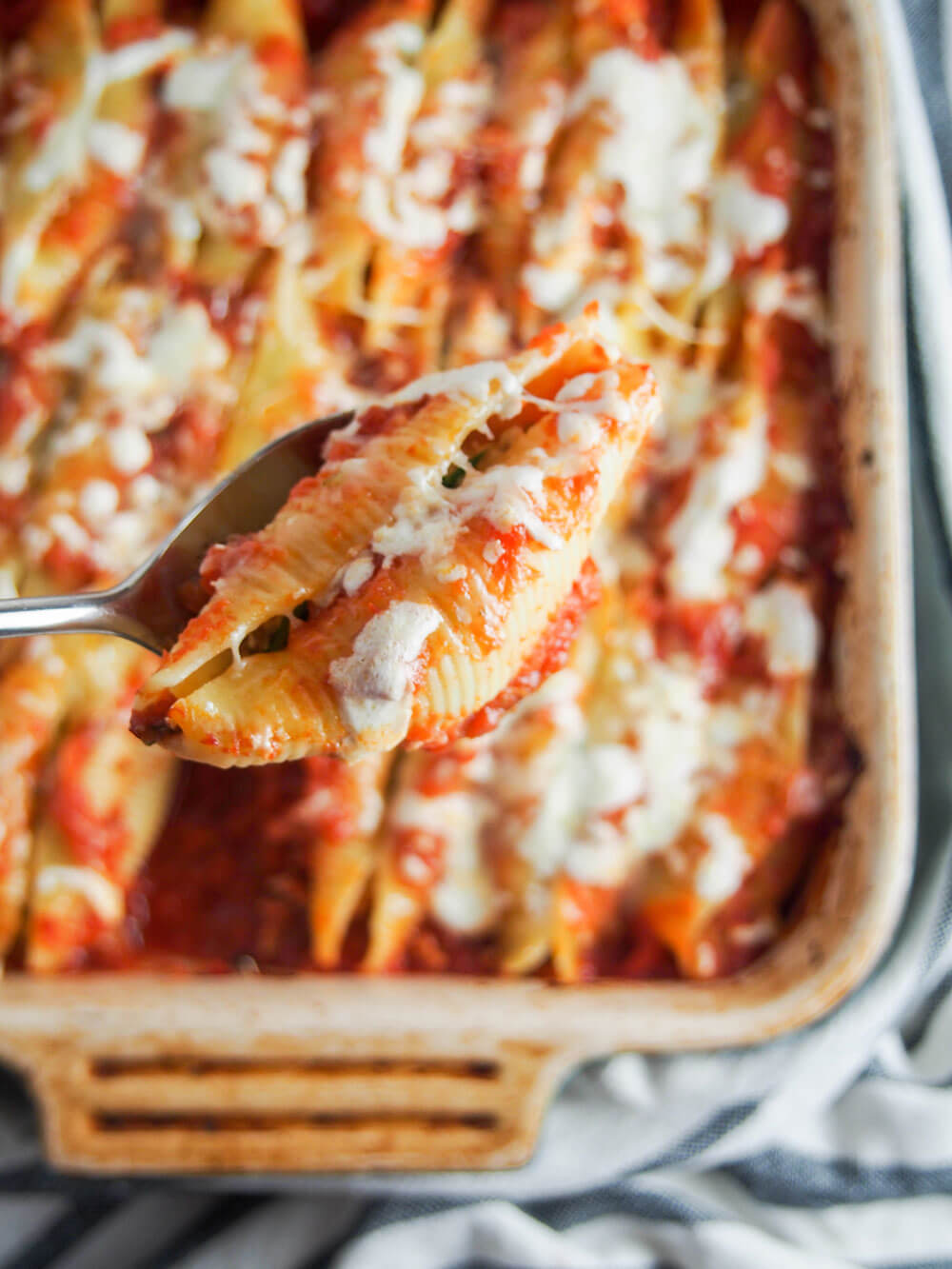 holding a pulled pork stuffed shell on spoon over dish