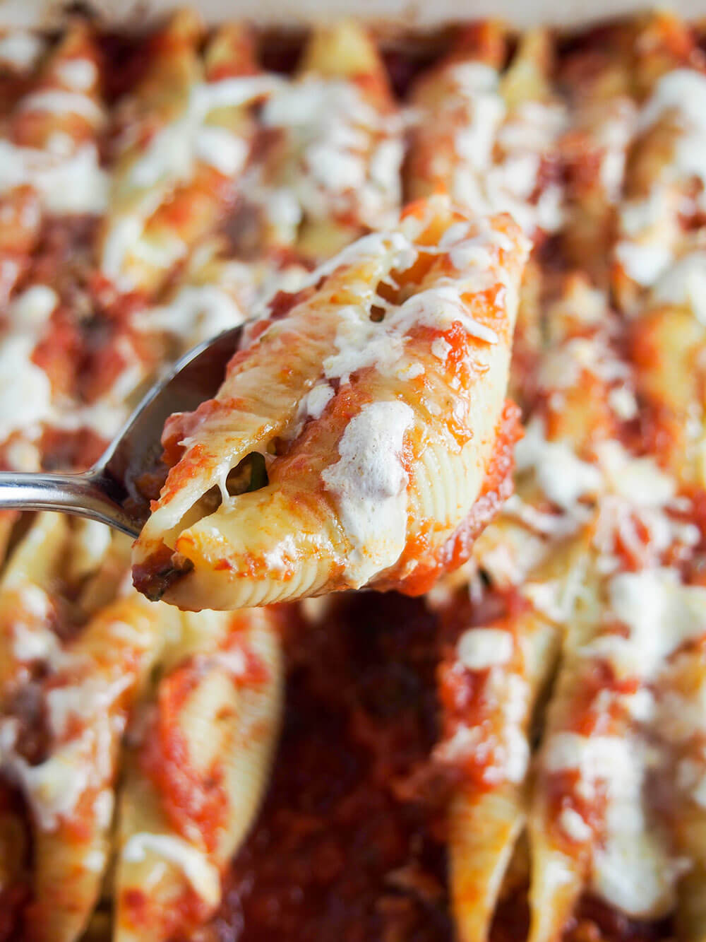 pulled pork stuffed shell held in spoon over dish with rest