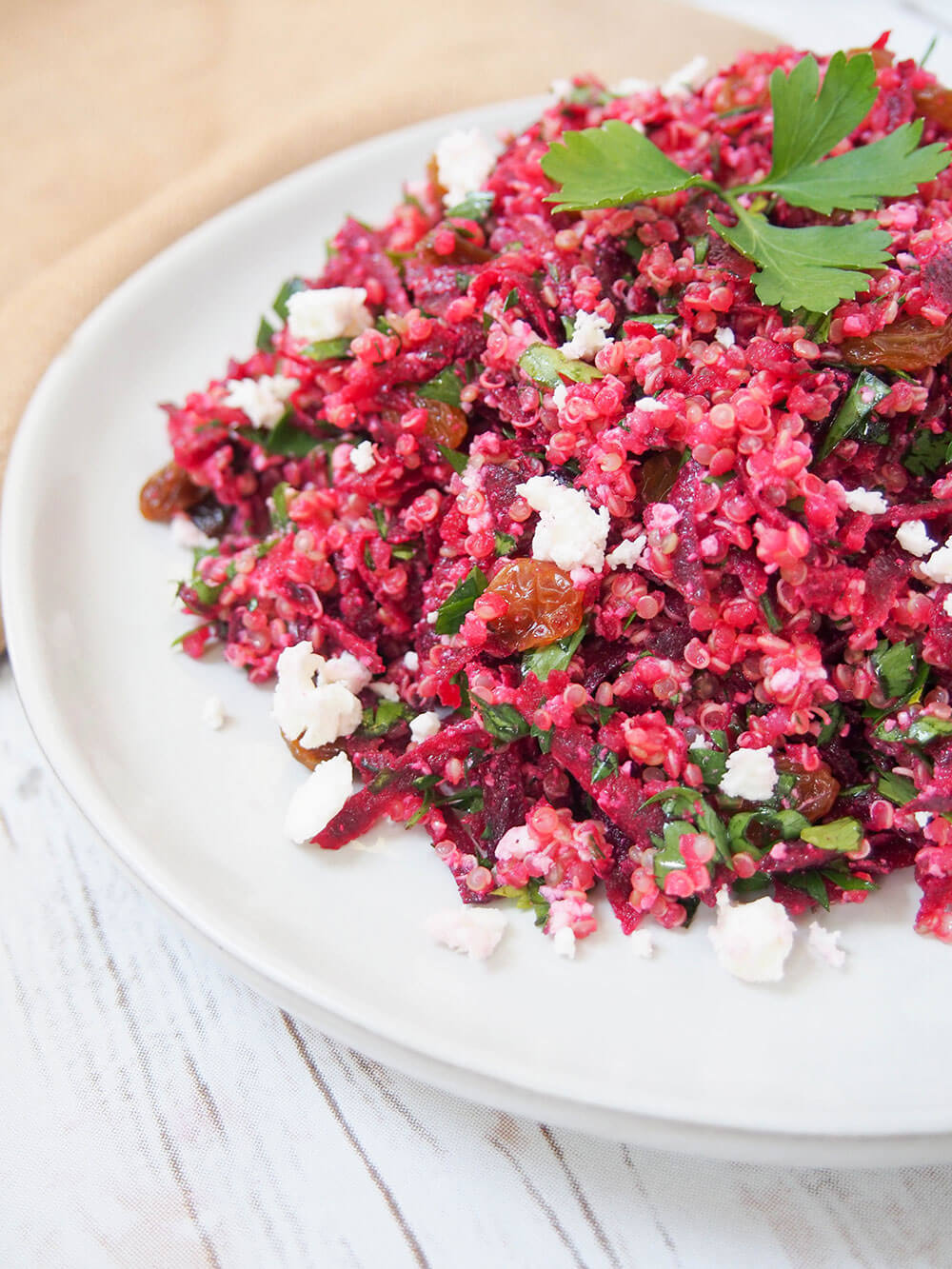 partial view of plate of raw beet quinoa salad topped with parsley sprig