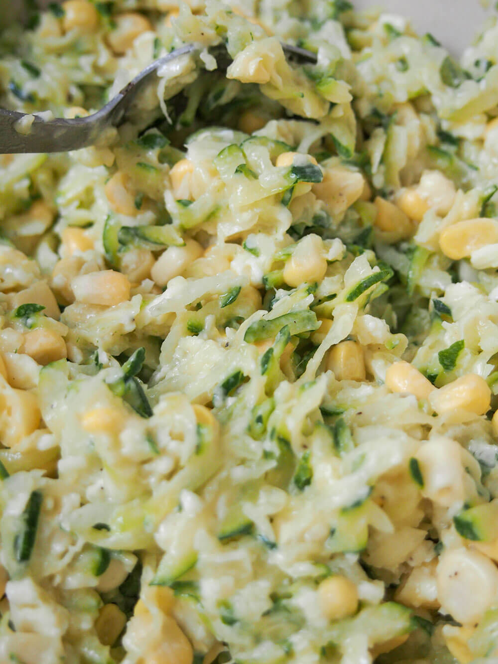 zucchini corn fritters mixture with spoon in bowl