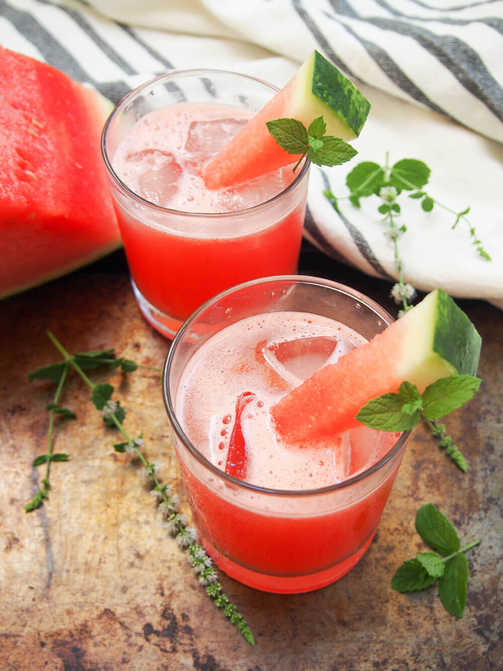 two glasses of watermelon coconut agua fresca with chunk of watermelon behind