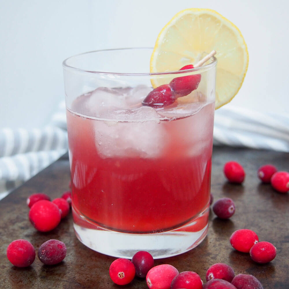 glass of cranberry whiskey sour with cranberries to side