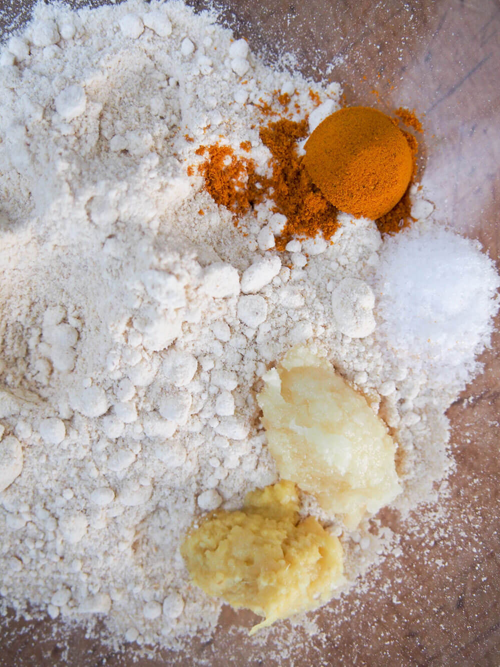 preparing batter for cauliflower pakora flour in a bowl with small piles of salt, turmeric, ginger and garlic on one side.