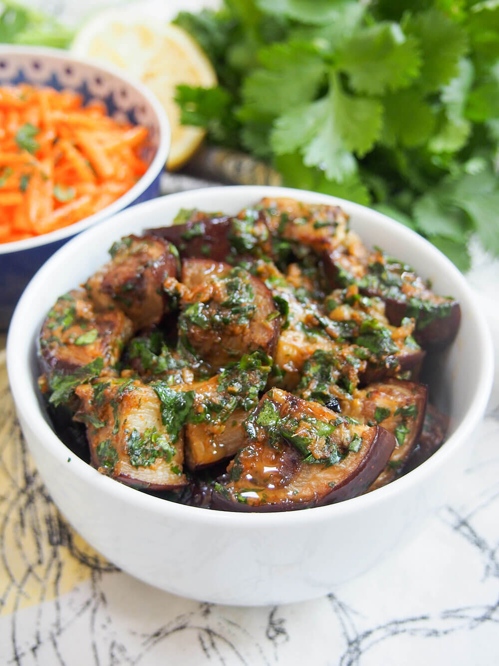 bowl of finished dish with carrot salad and cilantro behind