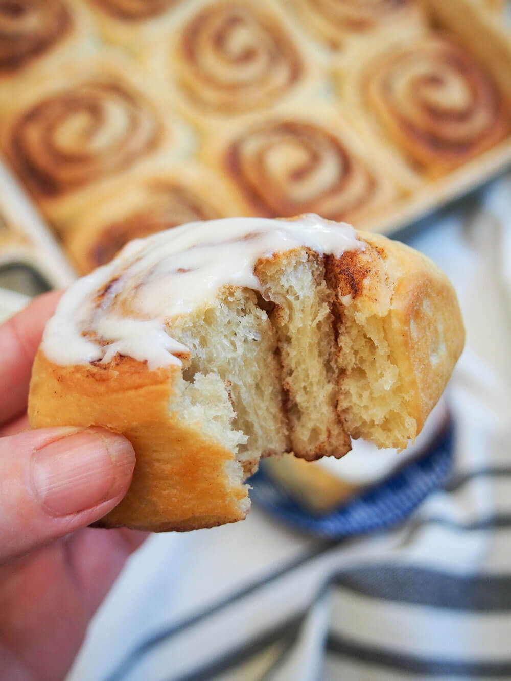eggnog cinnamon roll with bite taken out held above dish with more