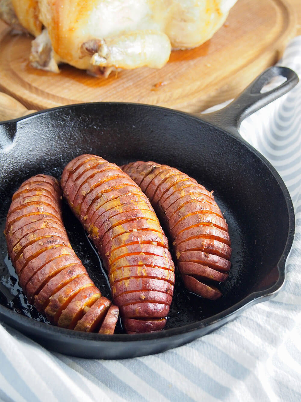 hasselback sweet potatoes in small skillet with roast chicken behind
