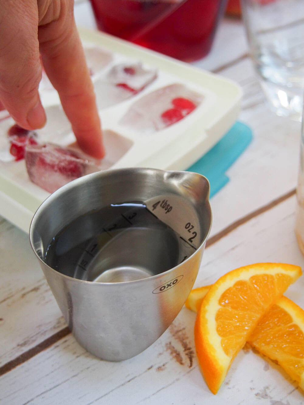 popping cranberry ice cube from ice cube tray with full jigger in front