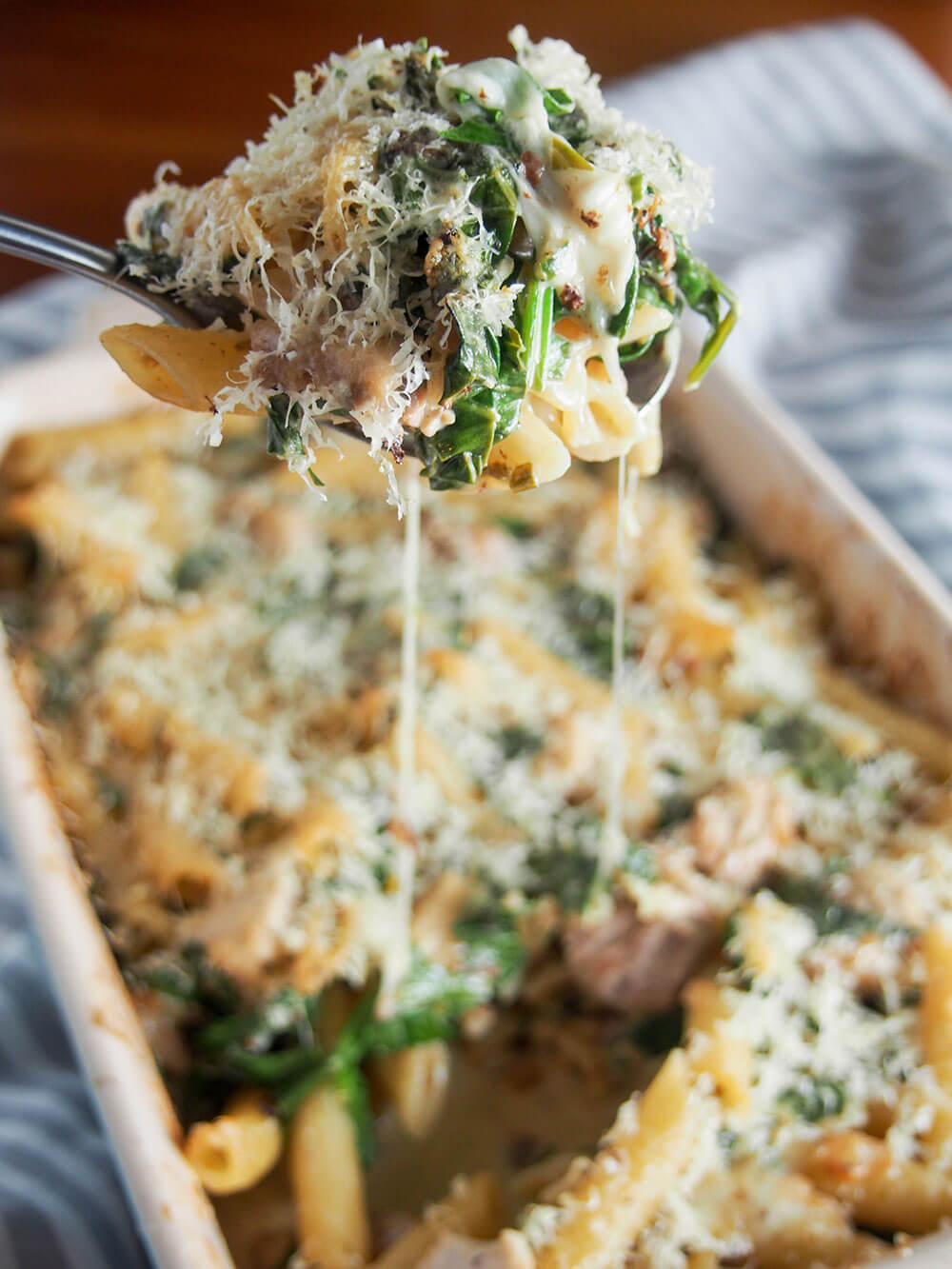 This creamy lemon chicken pasta bake has so much tastiness going on from the tarragon lemon cream sauce that wraps together the pasta, chicken and spinach. cheese pull from spoonful of pasta held over dish