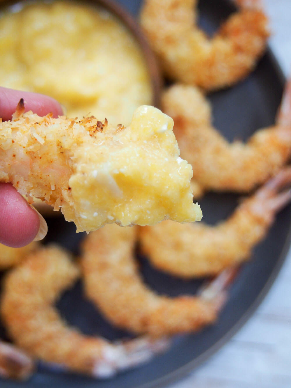 holding bite of Baked coconut shrimp with mango dipping sauce on it