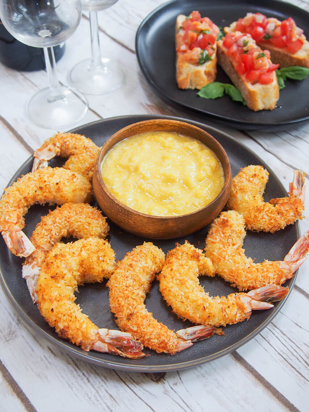 plate of coconut shrimp with glasses and bruschetta behind