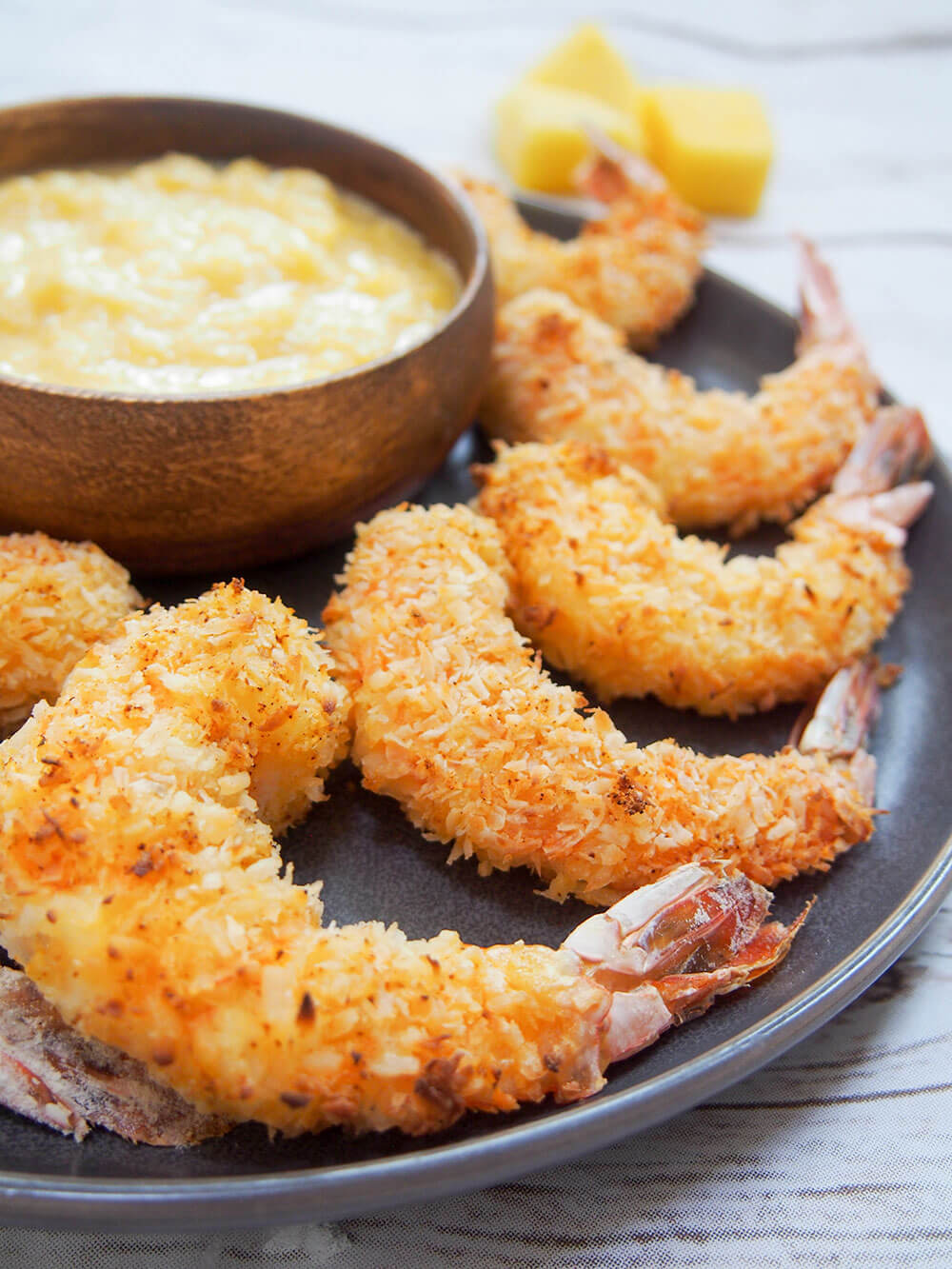 close up of baked coconut shrimp with mango dipping sauce behind