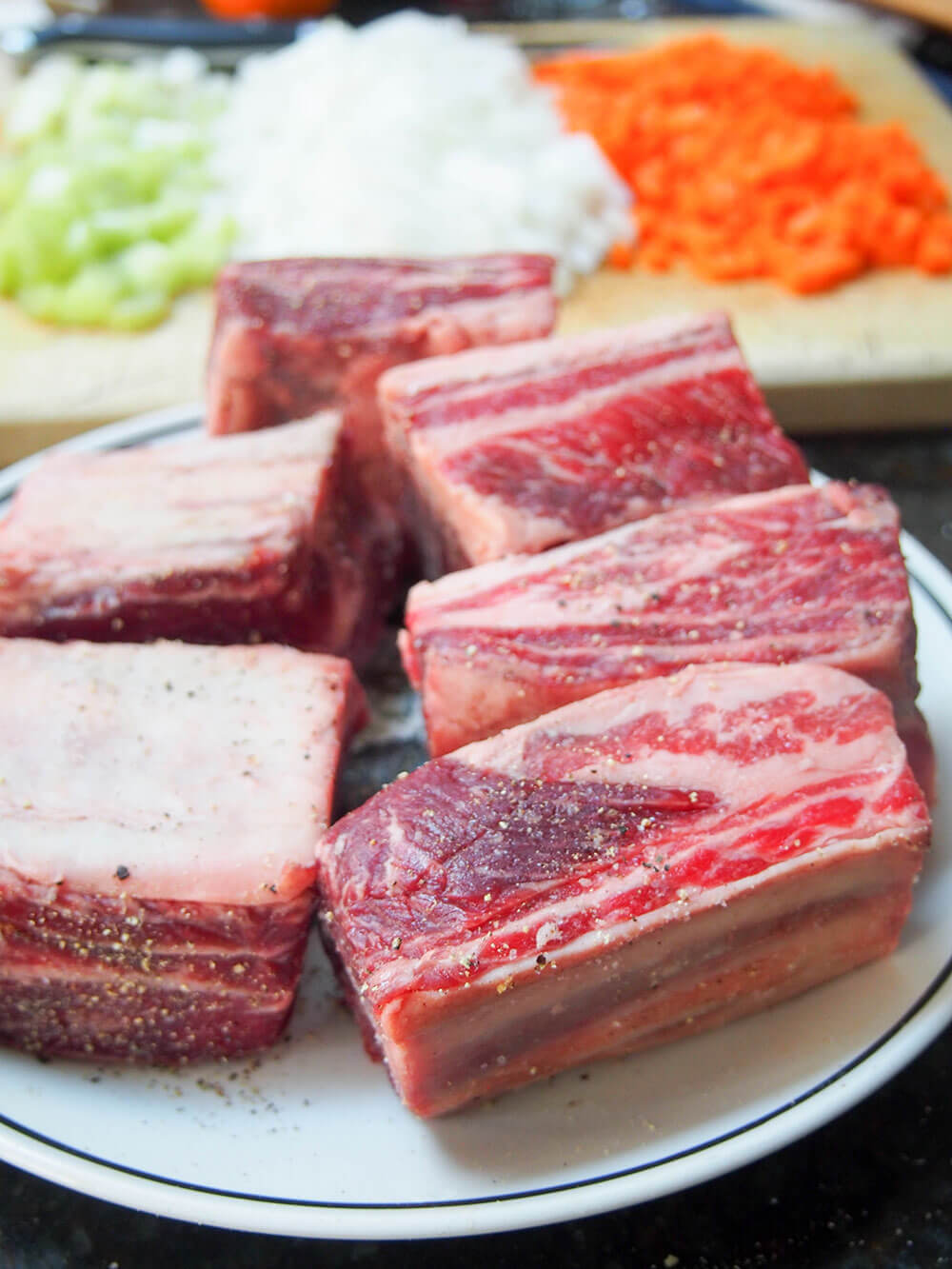 seasoning short ribs with salt and pepper with ingredients for sauce behind seasoning short ribs with salt and pepper with ingredients for sauce behind