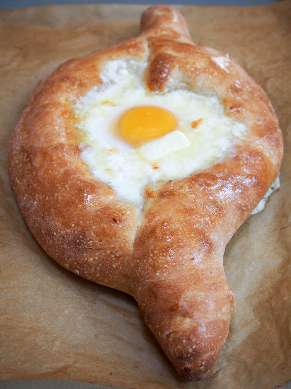 adding butter to middle of baked Adjaruli khachapuri Georgian cheese bread