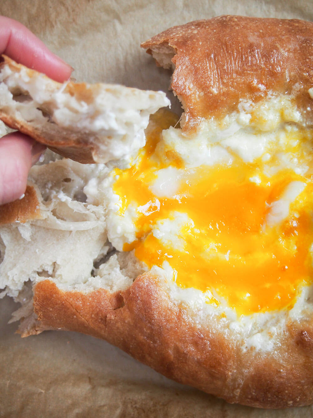 tearing piece from Adjaruli khachapuri  and dipping the bread into the cheese and egg filling