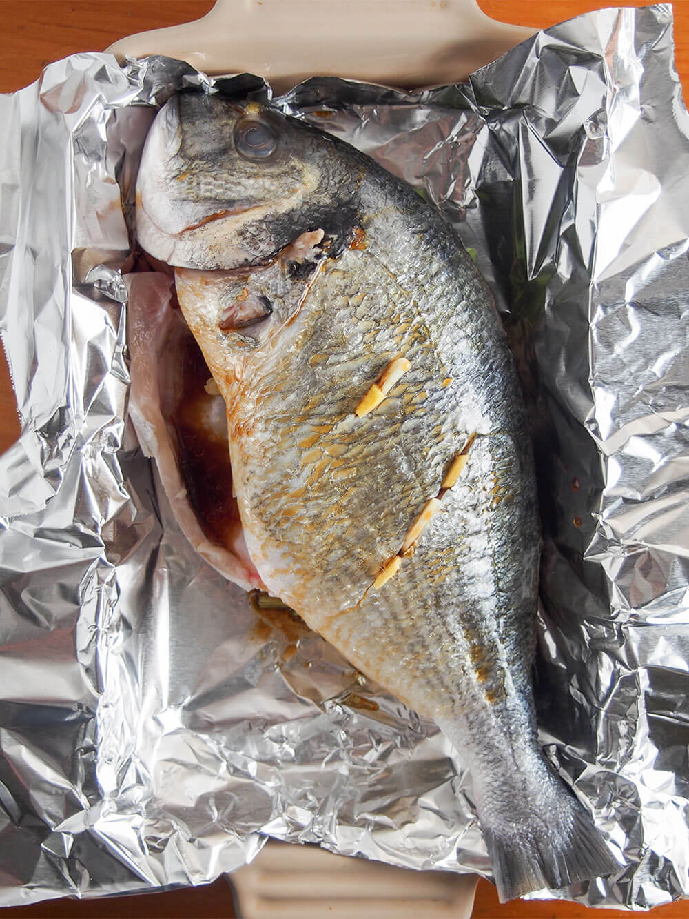 fish with pieces of garlic in slits in skin and light dressing over top before cooking