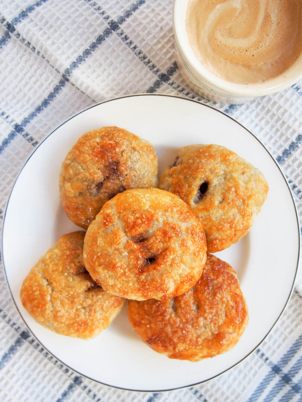 Eccles cakes may look a bit unassuming on the outside, but that pastry is wonderfully rich and crisp with a sticky, gently spiced fruity filling. These are a British treat you need to try! plate of Eccles cakes from above with cup of coffee in top right