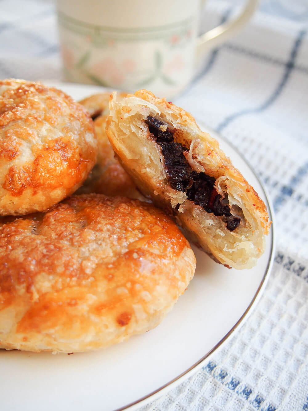 Eccles cakes may look a bit unassuming on the outside, but that pastry is wonderfully rich and crisp with a sticky, gently spiced fruity filling. These are a British treat you need to try! Eccles cakes - crisp currant filled pastries with one broken open resting next to others