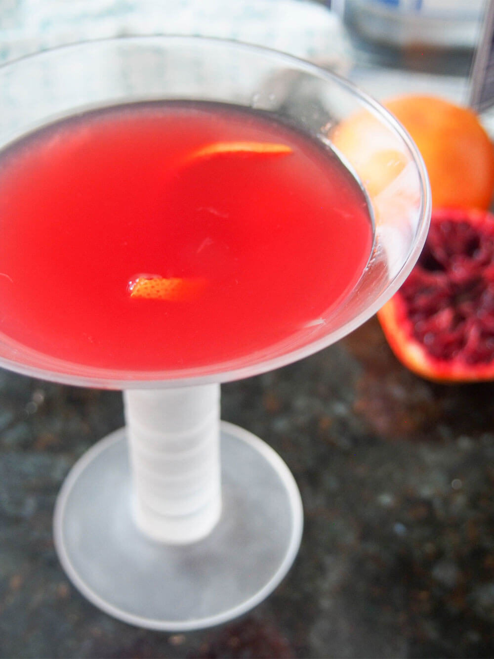 glass of blood orange bees knees cocktail from side with blood orange behind