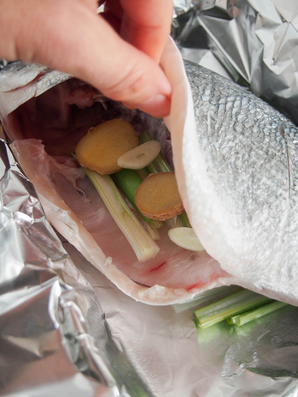 adding spring onion, garlic and ginger slices to cavity in fish