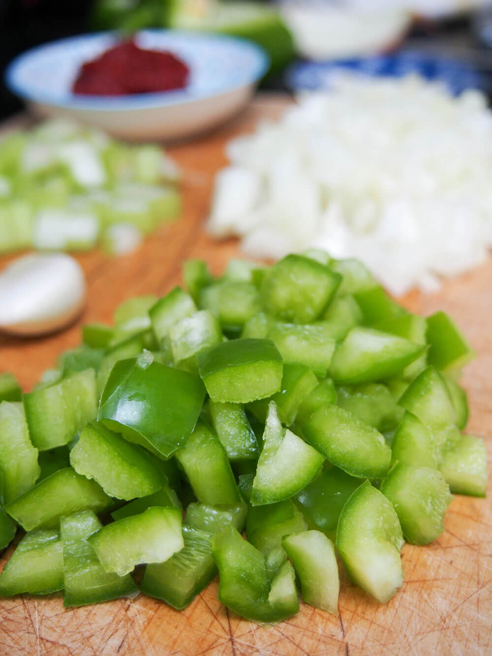 chopped up green pepper on chopping board with onions and celery blurred behind
