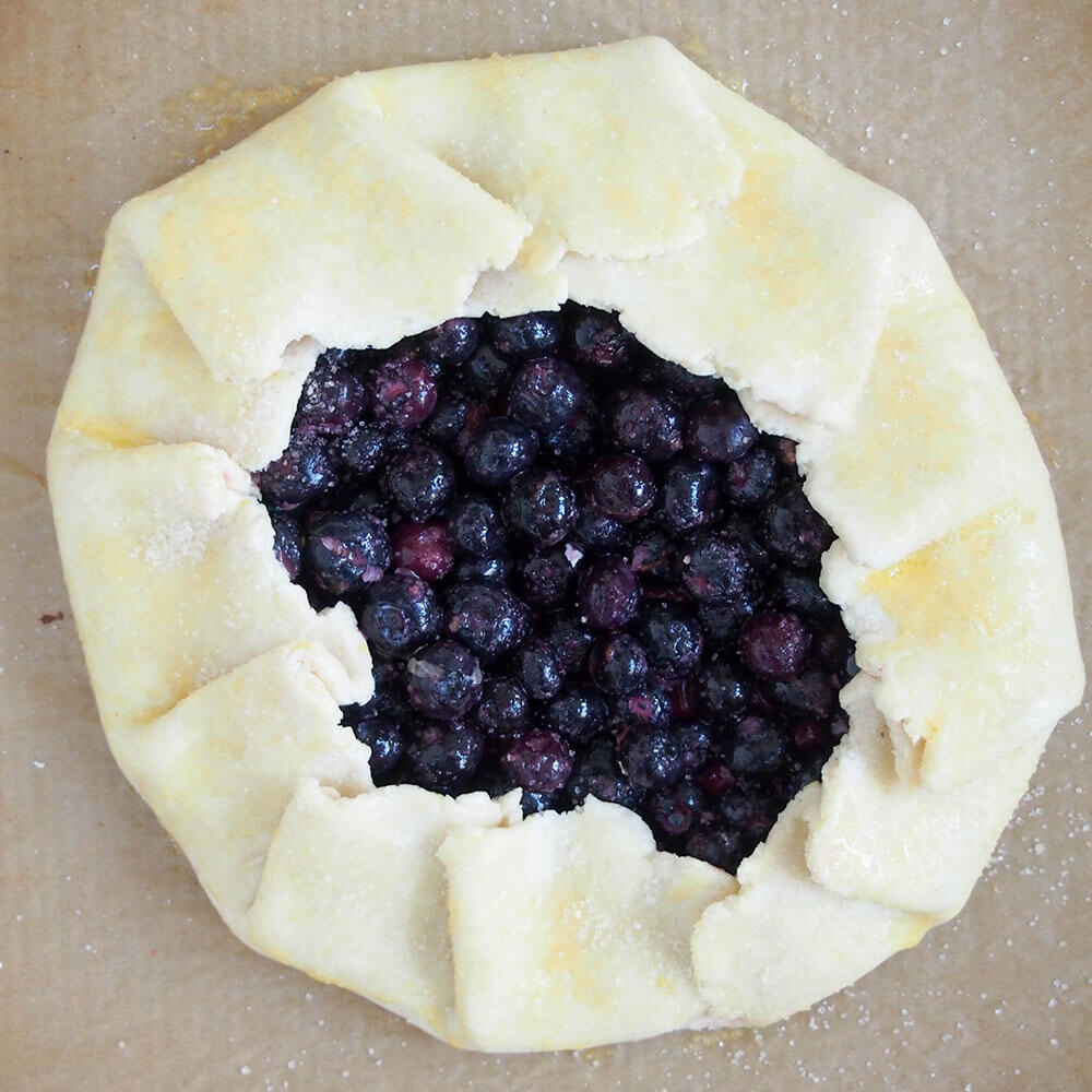 blueberry galette ready to bake, with sides folded in and egg wash on pastry