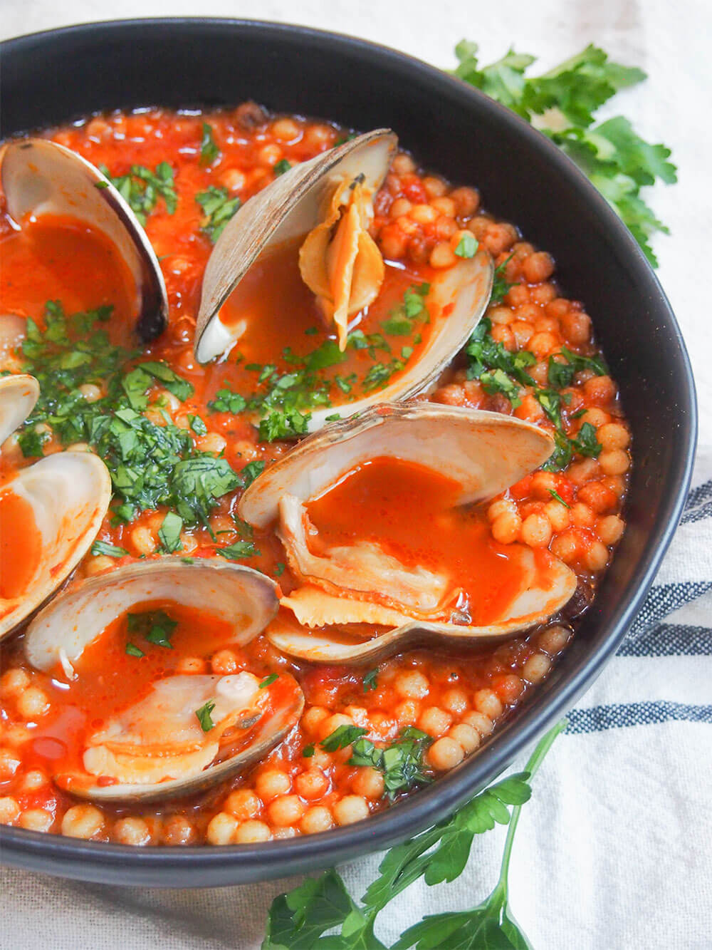 partial view of fregola with clams in black bowl, topped with parsley