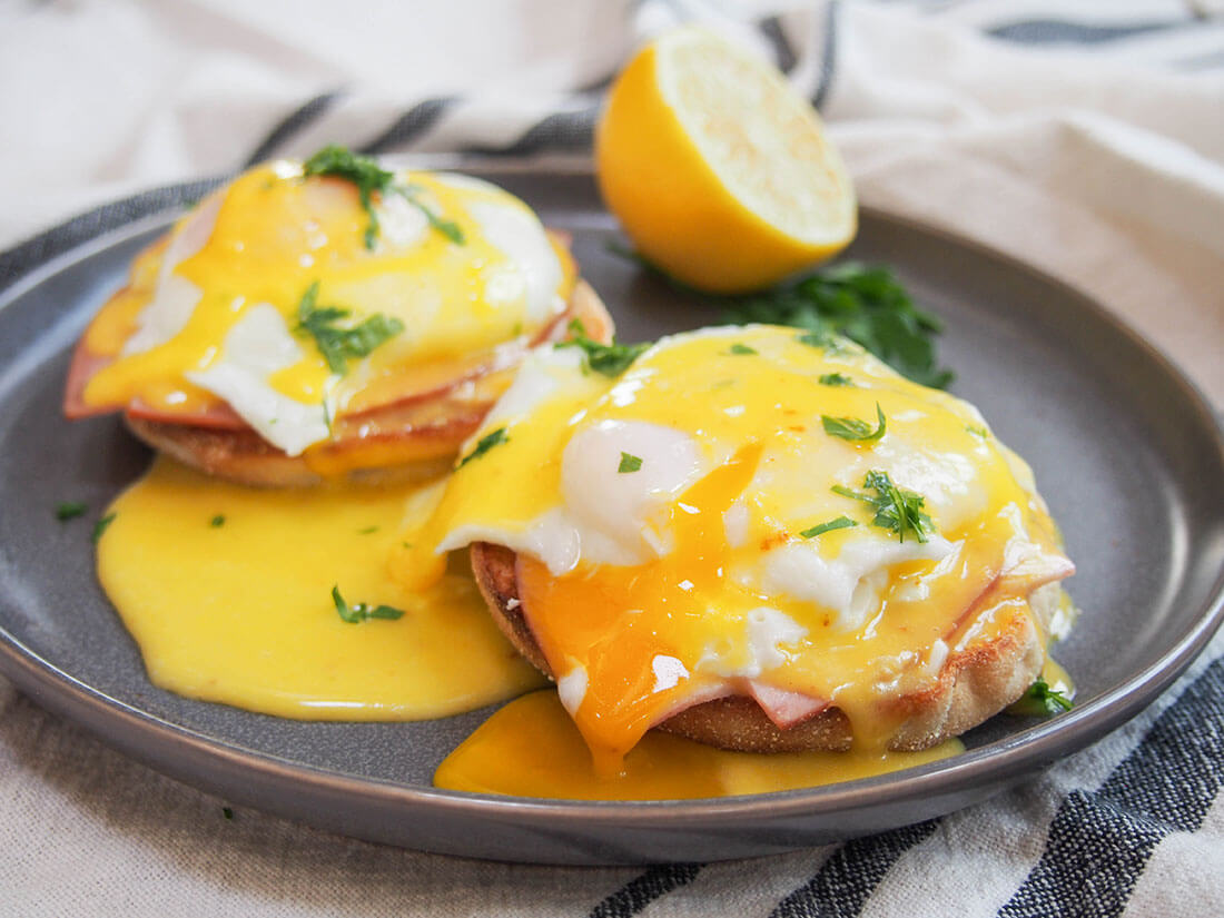 eggs Benedict on plate with yolk oozing into sauce