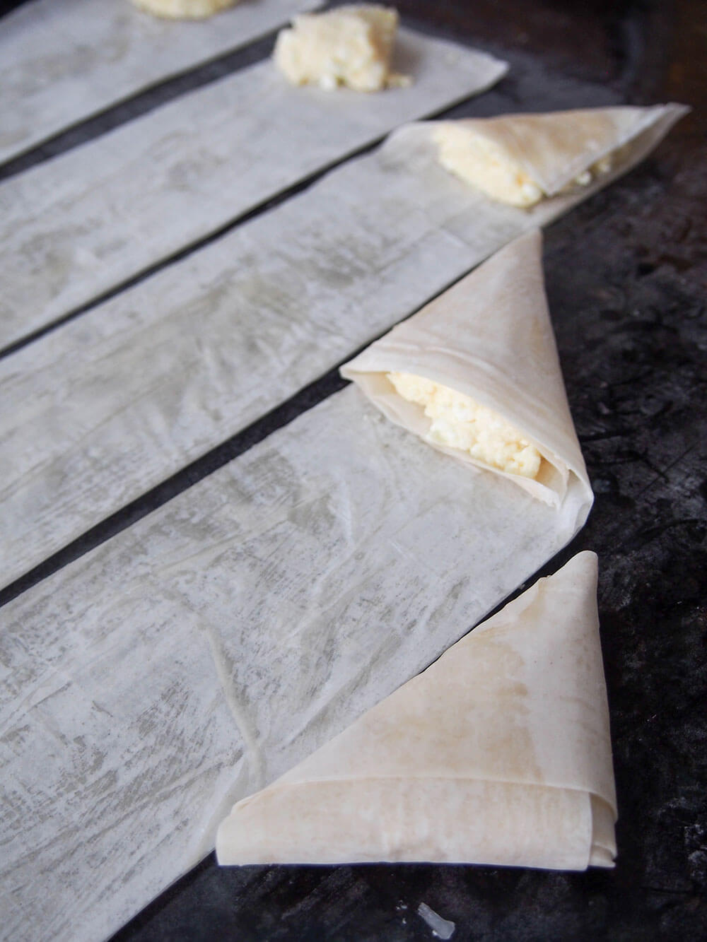 different stages of folding tiropita in filo pastry triangles