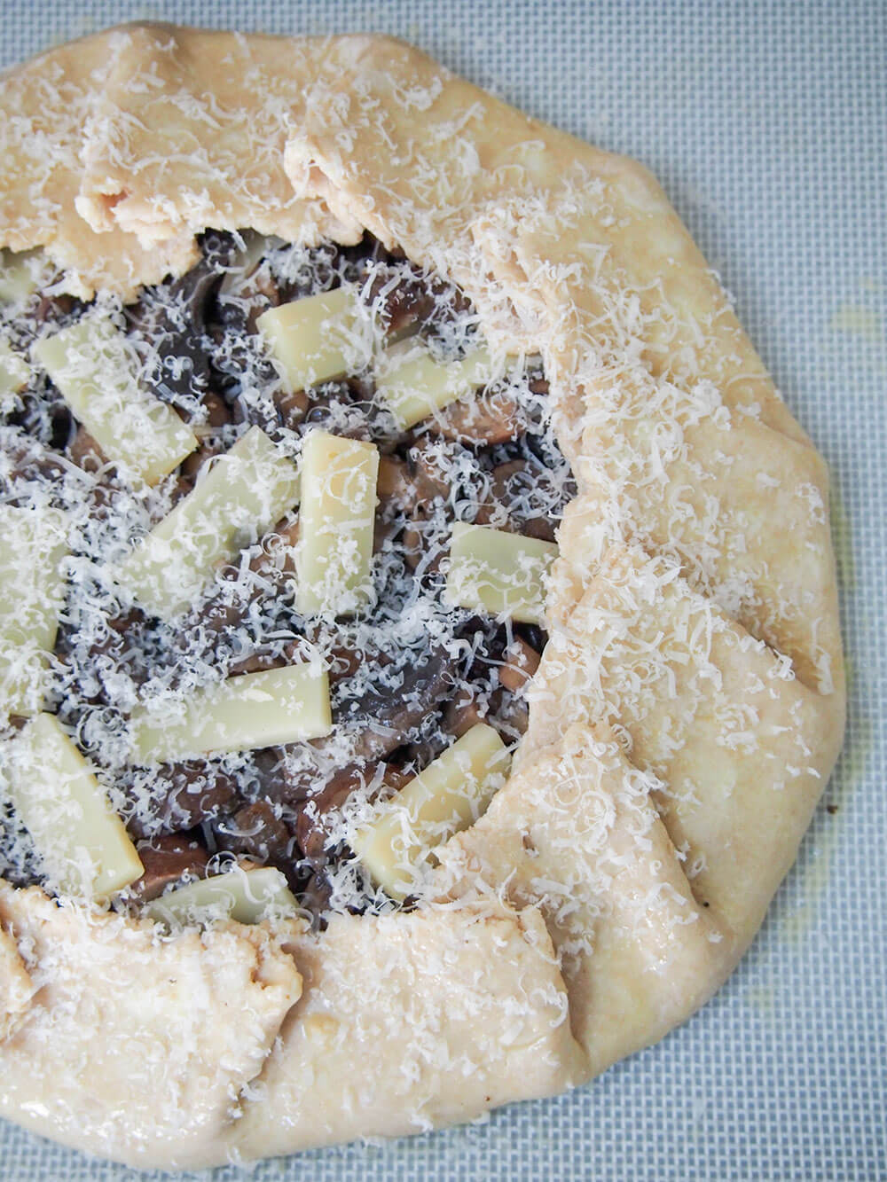 galette toped with pieces of fontina cheese and grated parmesan ready to bake