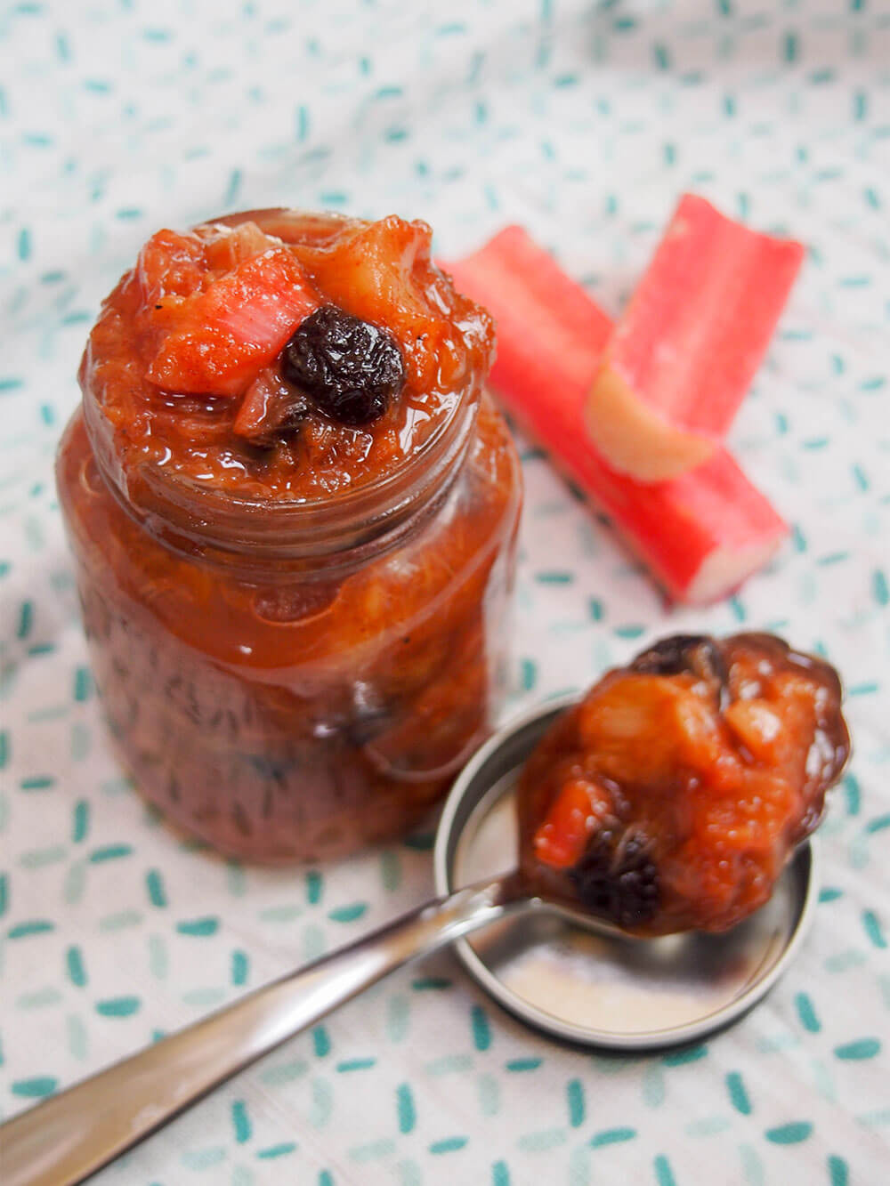 rhubarb chutney in jar with spoon of chutney resting on lid to side